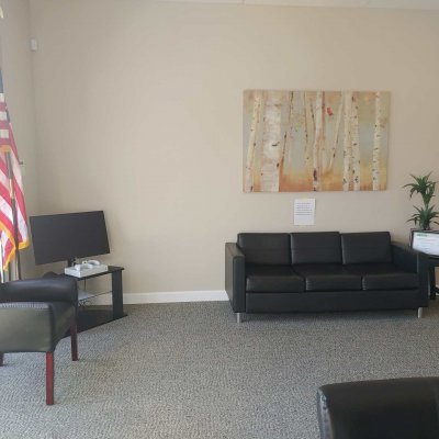 waiting area with a TV, xbox, sofa, chair, plant on a small table, artwork on the wall, and an American flag