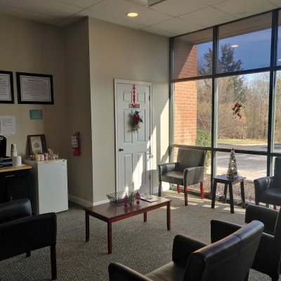 waiting area with chairs, a table, coffee bar and large windows to a parking lot