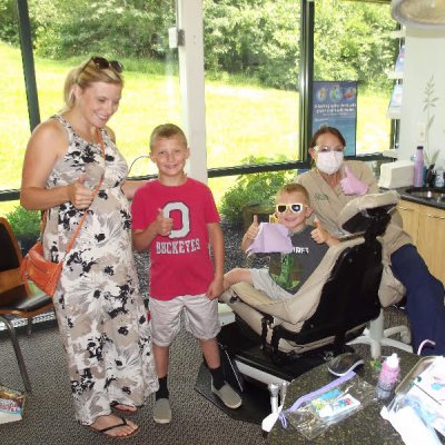 family smiling with an employee in a dental room with large windows and a chair